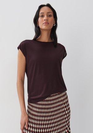 Donker bordeaux kortekorte top met een relaxte pasvorm, gecombineerd met een patroonrok met rode, crèmekleurige en zwarte ruitvormen.