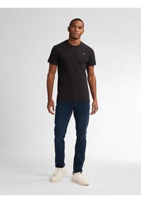 Czarna koszulka z krótkim rękawem i okrągłym dekoltem, zestawiona z ciemnoniebieskimi dżinsami i jasnymi trampkami, z logo na piersi.