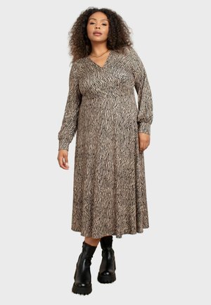 Langsleeve wikkeljurk in beige met zwarte zebraprinten, met een getailleerde taille en een vloeiende rok, gecombineerd met zwarte stevige enkelboots.