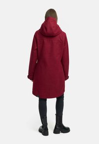 Burgundowy płaszcz z mieszanki wełny z dużym kapturem, długimi rękawami i zapięciem na napy, zestawiony z czarnymi dopasowanymi spodniami i botkami za kostkę.