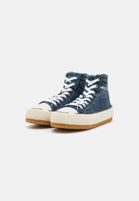 Des baskets montantes avec une tige en denim, des lacets blancs et une semelle en caoutchouc beige avec un motif texturé et un empiècement de protection à l'avant.