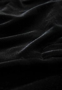 Tessuto di velluto nero con una texture morbida e liscia, caratterizzato da morbide pieghe e ondulazioni, che cattura la luce in modo sottile sulla sua superficie.
