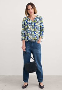 Top con motivo a righe con design astratti blu, verde e bianco; jeans in denim; borsa a tracolla nera; ballerine scure; vestibilità comoda.