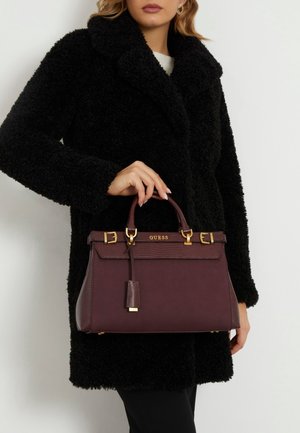 Burgundy handbag with textured sides, gold hardware, and a detachable charm. Features a structured shape and top handles for carrying.