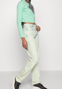 Mint green long-sleeve crop top paired with light green high-waisted jeans featuring turquoise stitching, worn with black platform sneakers.