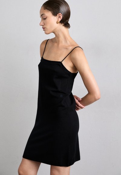 Abito nero aderente con spalline sottili, dal design fitted e con una consistenza morbida. Presenta una silhouette minimalista e un sottile logo sul lato.