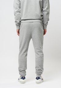 Pantalones de chándal de mezcla de algodón gris con una cinturilla elástica, piernas ajustadas y puños acanalados. Combinados con zapatillas blancas con detalles en azul marino y rojo.