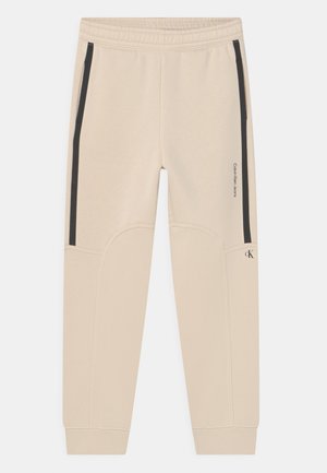Beige Calvin Klein joggingbukser med sorte lodrette striber på siderne, elastisk talje, manchetter ved anklerne og lille logo på højre ben.