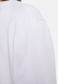 Pull léger lavande présentant un tissu lisse et texturé, des détails de coutures visibles, et une coupe décontractée avec une épaule légèrement baissée.