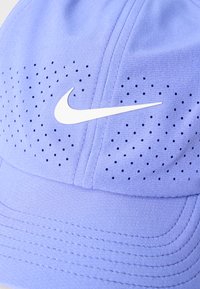 Ανοιχτό μωβ καπέλο με μικρές τρύπες αερισμού και λευκό λογότυπο Nike swoosh στην μπροστινή πλευρά πάνω από τη γείσο.