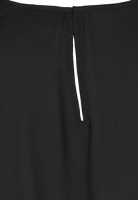 Svart plagg med en slät textur, en nyckelhålsöppning på baksidan och snygg sömnad längs kanterna.