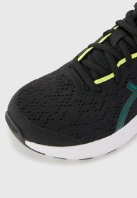 Chaussure de course noire avec empeigne en mesh texturé, accents verts, semelle blanche contrastante et lacets plats, conçue pour le confort et la respirabilité.