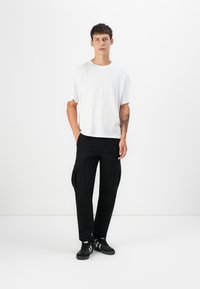 Hvid bomulds t-shirt, afslappet pasform, kombineret med sorte cargo bukser med sidelommer. Sorte sportssko fuldender outfittet.