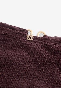 Paarse gaasstof met een gestructureerd diamantpatroon. Voorzien van een logo en hardware in goudkleur. Zacht en flexibel materiaal met accenten.