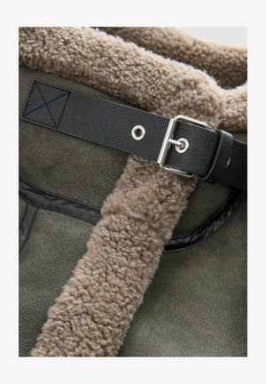 Close-up of gray shearling coat with soft wool lining and black leather strap secured by silver buckle.