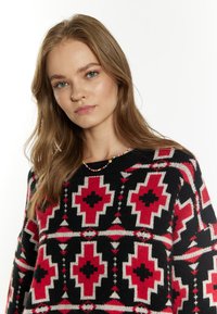 Gebreide trui met een geometrisch patroon in rood, zwart en wit, met een ronde halslijn en een relaxte pasvorm. Aangevuld met een multikleurige kralenketting.