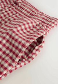 Červená a béžová kockovaná látka s mäkkou textúrou a elastickým pásom. Obsahuje bočnú kapsu a mierne zahnutý lem.