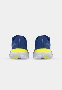 Chaussures de sport bleues avec un accent jaune au talon, tige en maille pour la respirabilité, et semelle extérieure blanche texturée. Vue arrière avec des détails de design minimalistes.