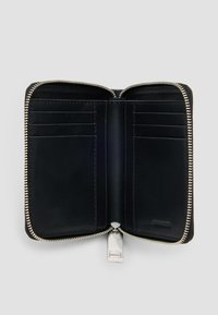 Cartera de piel negra con cierre de cremallera alrededor. El interior cuenta con múltiples compartimentos para tarjetas y una textura suave. Detalle de hardware en plata en la parte inferior.