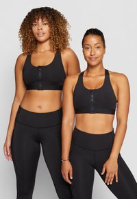 Sutiãs desportivos pretos com fechos éclair na frente, combinados com leggings pretas de cintura alta. Tecido liso e design simples, sem padrões ou aplicações.