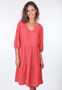 Kleid aus Korallenleinen mit V-Ausschnitt, dreiviertel puffärmel und einem gestuften Rock. Auffällige Spitzenverzierungen entlang des Ausschnitts und des Saums.