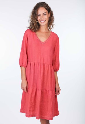 Kleid aus Korallenleinen mit V-Ausschnitt, dreiviertel puffärmel und einem gestuften Rock. Auffällige Spitzenverzierungen entlang des Ausschnitts und des Saums.