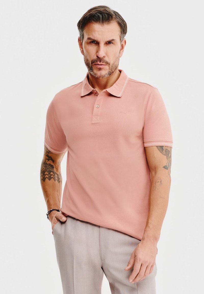 Różowa koszulka polo z kołnierzykiem, krótkimi rękawami i kontrastowym paskiem. Bawełnowy materiał, dopasowany krój, w połączeniu z jasnymi spodniami.