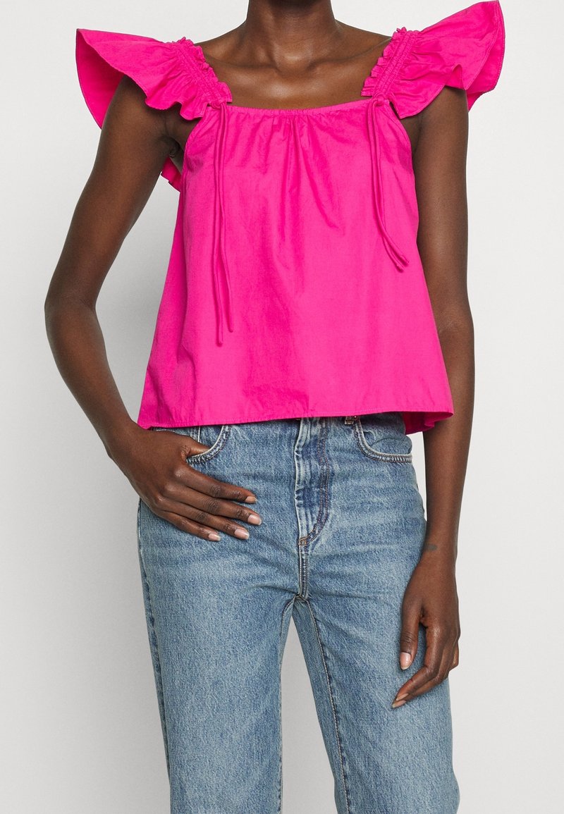 Top de algodón fucsia con mangas rizadas sin hombros, escote con cordón y un ajuste holgado, combinado con unos jeans de tiro alto en azul claro.