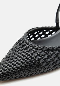 Μαύρο πλεκτό παπούτσι με μυτερή μύτη, πλεγμένα δερμάτινα λουριά και λουρί για τη φτέρνα.