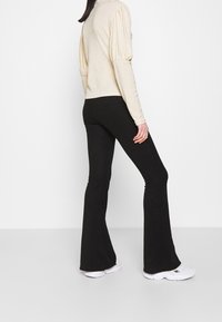 Kermakudu dengan lengan menggelembung dipadukan dengan celana flare hitam bergaris. Sepatu sneakers putih menyempurnakan penampilan.