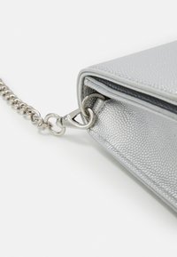 Silver textured handbag corner with silver chain strap attached by metal clasp on white background.