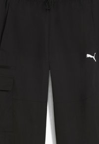 Czarne spodnie cargo z elastycznym pasem, sznurkiem, bocznymi kieszeniami oraz białym logo Puma. Materiał wydaje się lekki i gładki.