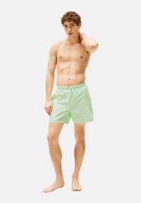Helle grüne Badeshorts aus leichtem Material, mit einem elastischen Bund und Kordelzug sowie einer Seitentasche.