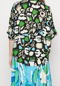 Maglietta nera a maniche corte con motivi organici multicolori che includono fiori, nuvole e uccelli. Vestibilità ampia con orlo arrotondato.