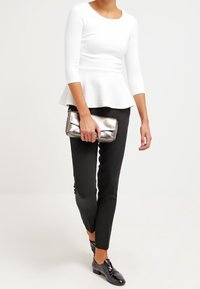 Weißes Peplum-Top aus strukturiertem Material, schwarze Slim-Fit-Hosen und eine metallische Clutch. Schwarze Lackschuhe runden das Outfit ab.