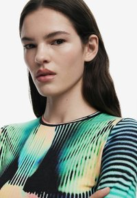 Bluză colorată cu un model ce prezintă nuanțe de verde, negru și portocaliu, cu dungi verticale și orizontale. Textură netedă, guler rotund.