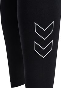 Zwarte leggings van rekbaar materiaal met drie witte chevronstrepen op de buitenkant van de dij, ontworpen voor comfort en beweging.