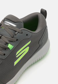Gray athletic shoe featuring a textured upper, green accents, silver logo, and a soft interior with a white rubber sole.