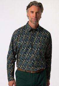 Námořnická košile s knoflíky a vzorem žlutých a oranžových listů; má rozšířený límec a dlouhé rukávy, doplněná zelenými kalhotami.