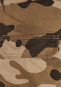 Close-up of brown and beige camouflage fabric with a rectangular stitched pocket flap.