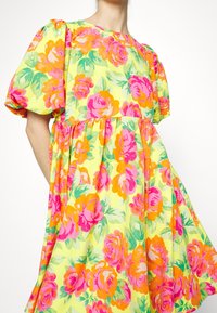 Blumenkleid mit gelbem Grundton und leuchtend pinken und orangenen Rosen. Puffärmel und eine geraffte Taille betonen die fließende Silhouette.