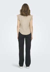 Haut beige clair avec des manches en dentelle et un ourlet arrondi, associé à un pantalon cargo noir avec des poches latérales et une coupe décontractée.