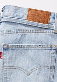 Lyseblå denimjeans har et skinnmerke med teksten "Levi Strauss & Co." med sømdetaljer og et lite rødt merke på siden.