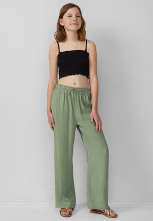 Zwarte smocked crop top gecombineerd met losse, lichtgroene broek; de broek heeft een elastische tailleband en een trekkoord; sandalen met dunne banden.