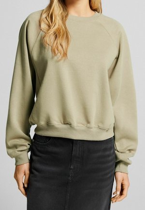 Sweatshirt en coton vert clair avec une coupe décontractée, des poignets et un ourlet côtelés, et des manches raglan. Associé à une jupe en denim noire.