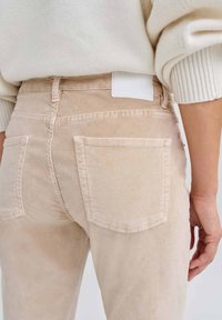 Hellbeige Cordhosen mit einem Design für die Gesäßtasche, featuring ein weißes Etikett am Bund. Der Stoff hat eine weiche, strukturierte Oberfläche.