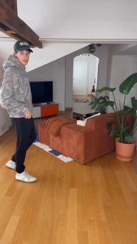 Sofá de veludo corduroy laranja com uma manta castanha, piso de madeira, planta verde em vaso e uma televisão montada na parede em um ambiente moderno.
