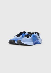 Blue athletic shoes with a textured mesh upper, black laces, a prominent logo, and a black rubber sole featuring traction nodes.