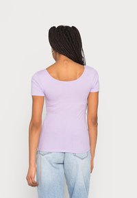 Lila ribbad topp med korta ärmar och skopad ryggdesign, tillsammans med ljusblå högmidjade jeans.