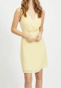 Vestido amarillo sin mangas con un diseño envolvente, cintura ajustada y textura suave. Largo hasta la rodilla con un acabado liso y sin patrones ni acentos visibles.